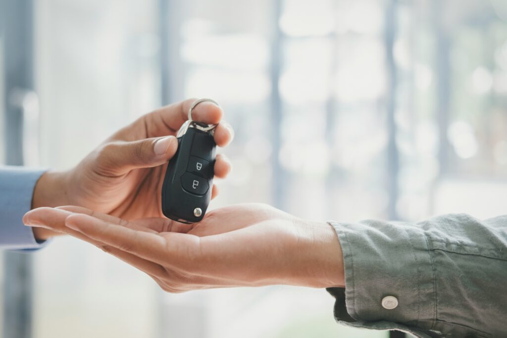 Close-up of a person handing over a car key to another person, symbolising car ownership, vehicle finance, or loan approval.
