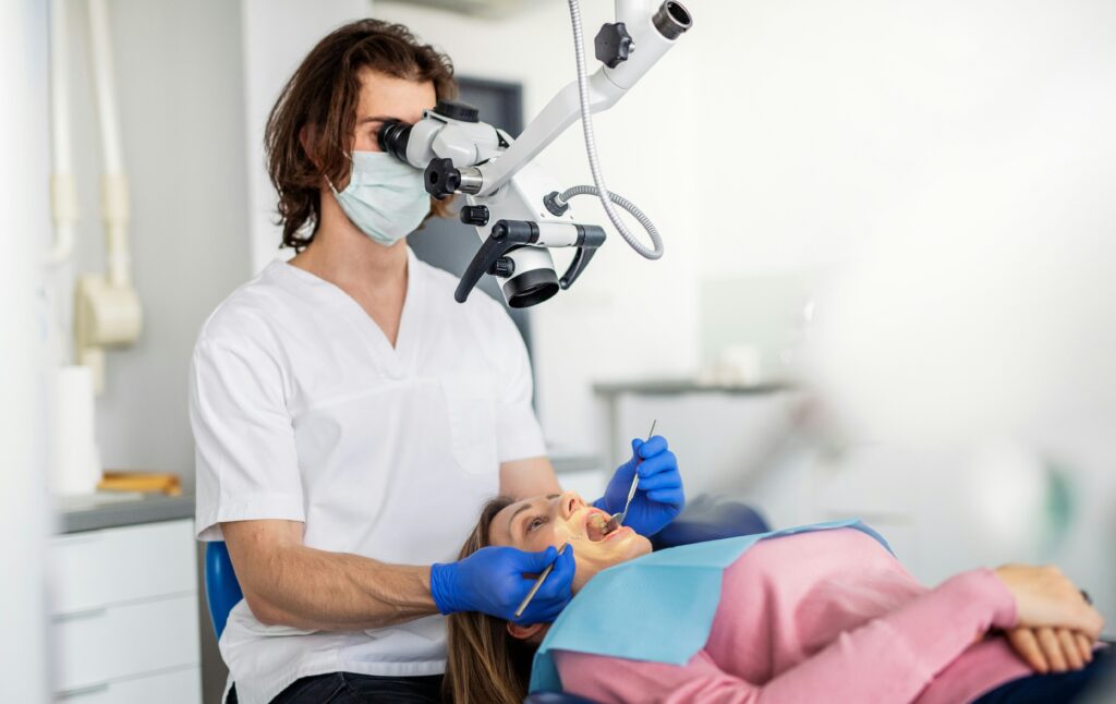 Dentist wearing a mask and gloves performing a dental examination on a patient in a modern treatment room using specialised equipment.
