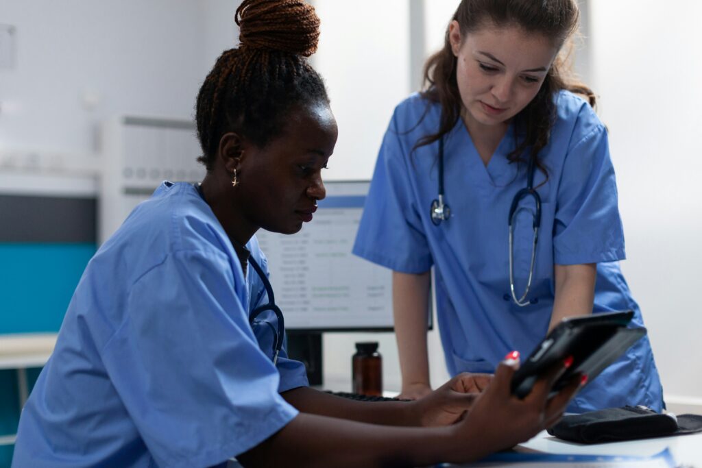 Two healthcare workers reviewing information on a tablet together at a hospital workstation.