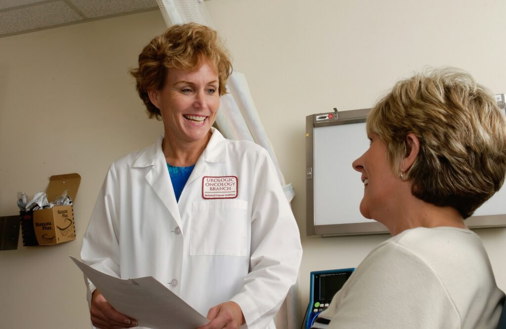 Doctor speaking with a patient during a medical consultation while holding paperwork in a clinic room.