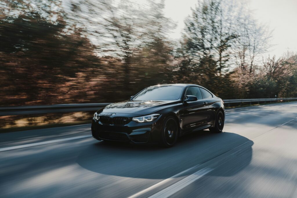 Black luxury sedan driving along a curved road surrounded by blurred trees, captured with motion blur to emphasise speed and movement. The image shows the car travelling on a sunny day with natural light reflecting off the vehicle, creating a sleek and cinematic road driving scene.