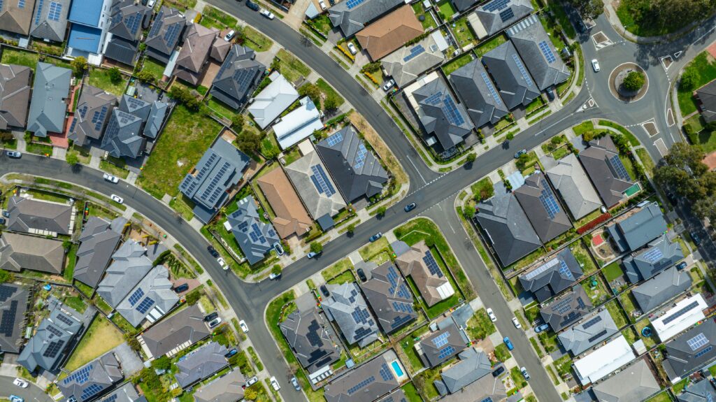 Aerial view of a suburban residential neighbourhood in Sydney, New South Wales, Australia, showing modern homes, curved streets, rooftops with solar panels, and surrounding greenery.